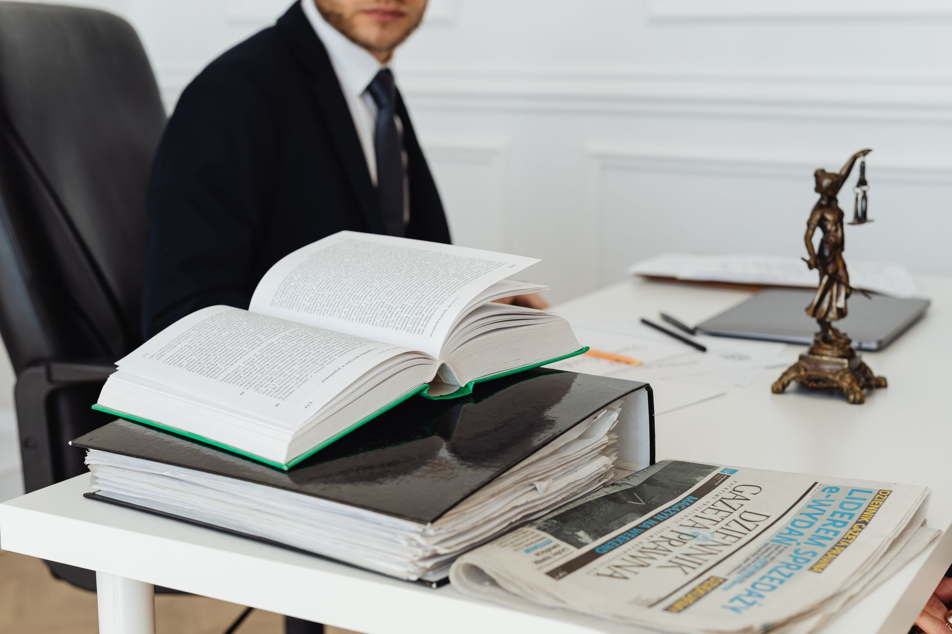 Homme en costume à un bureau avec code juridique ouvert, classeurs, journal et statuette de la justice