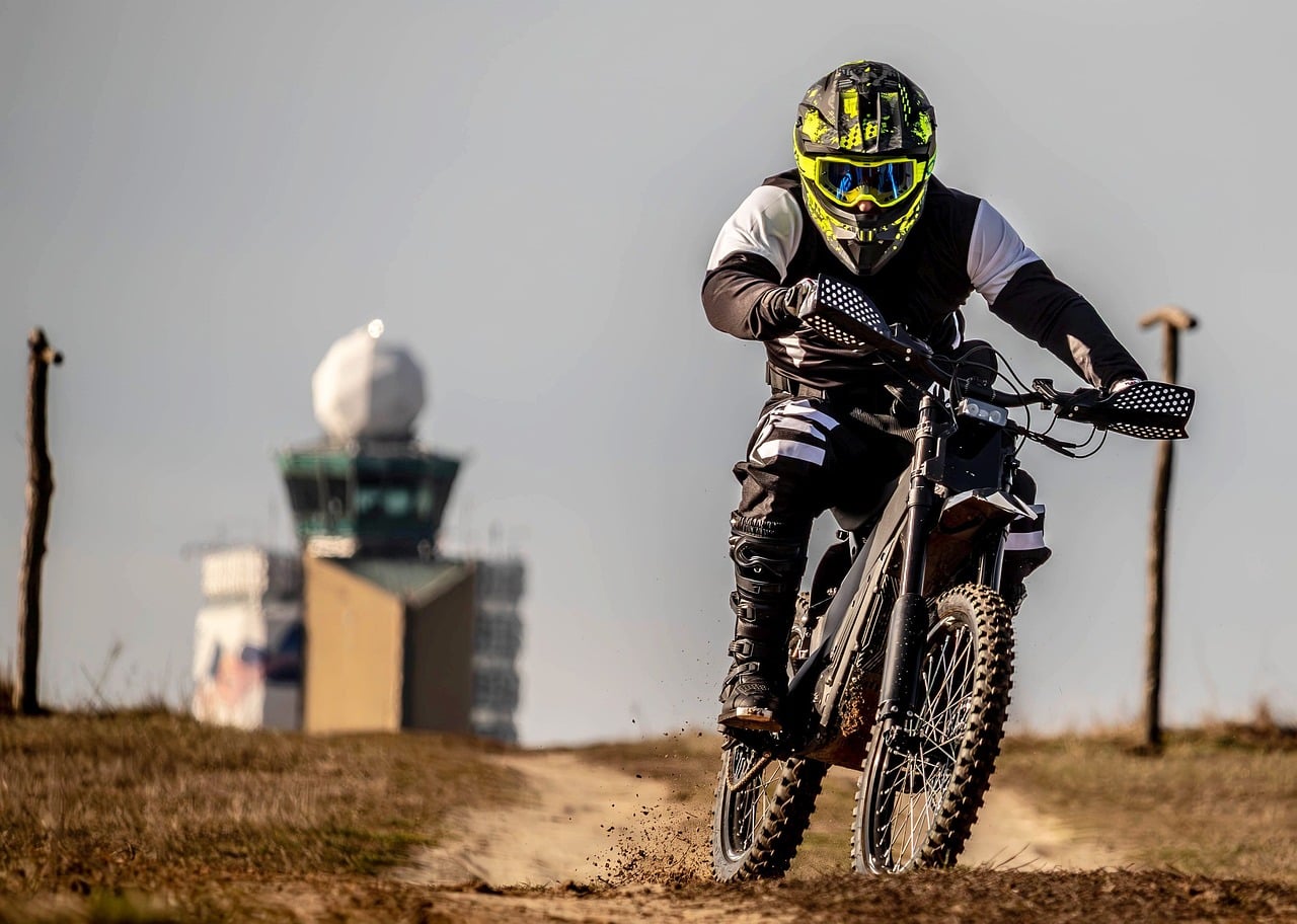Pilote de moto casqué, vu de face sur un chemin de terre, au guidon d'une moto tout-terrain noire qui soulève un peu de terre